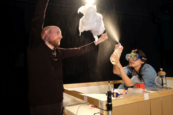 Schauspieler hält eine Wolke aus Watte und Schauspielerin mit Schwimmbrille besprüht die Wolke mit einem Pumpspray.